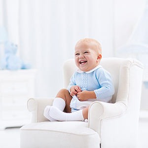 Happy child relaxing in toy chair on play mat. Nursery and play room for young children. Infant furniture, clothing, texti