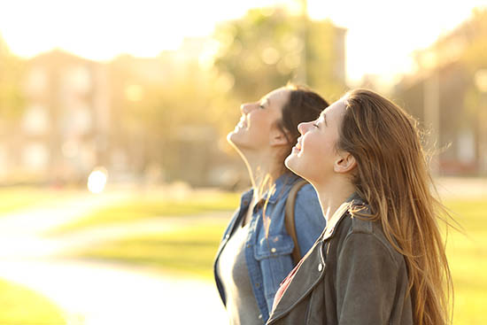 Side view portrait of two happy girls breathing fresh air together in a park at sunset with a warm back light in the background