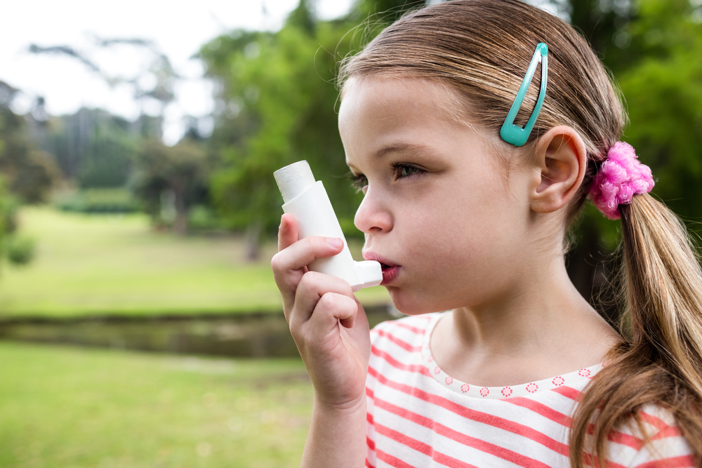 Girl using an asthma inhaler in the park