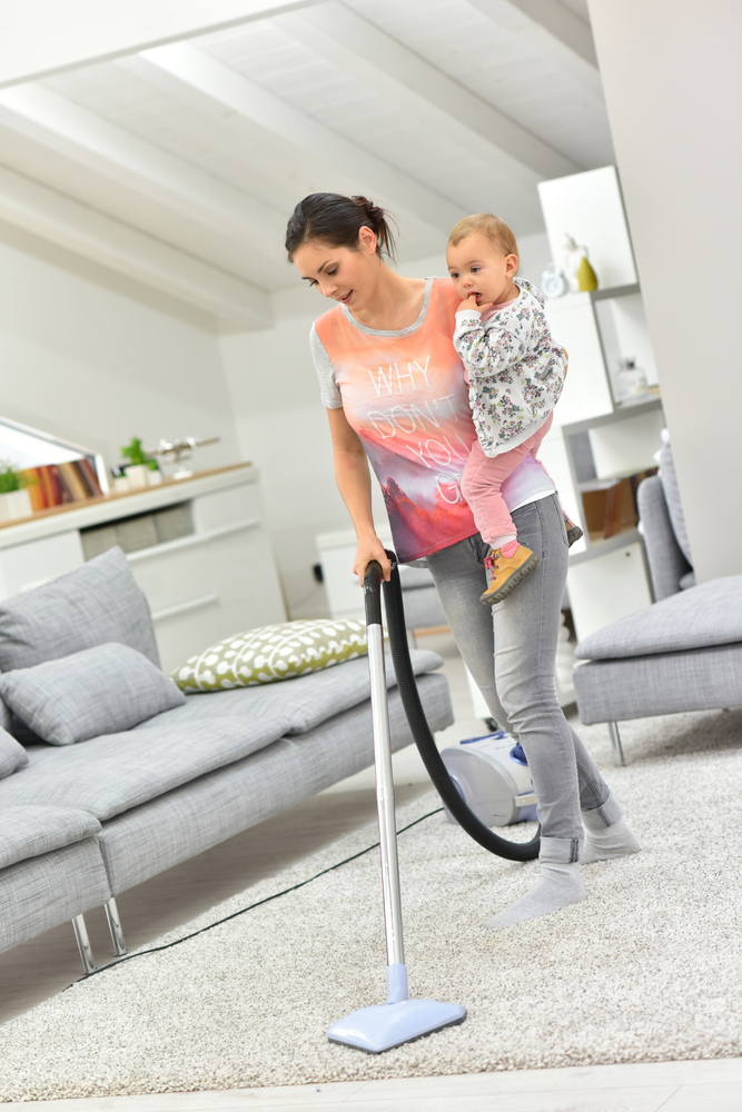 Mother vacuum cleaning floor with baby in arms