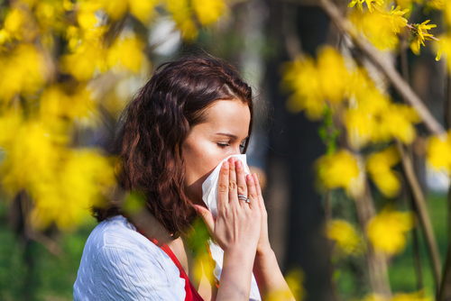 woman blowing nose standing by flowers